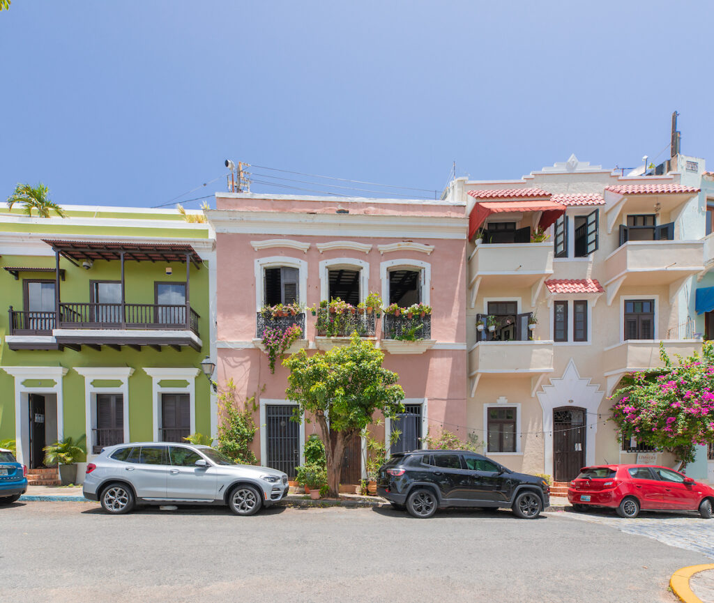 Cars in front of a row of pastel colored old buildings.