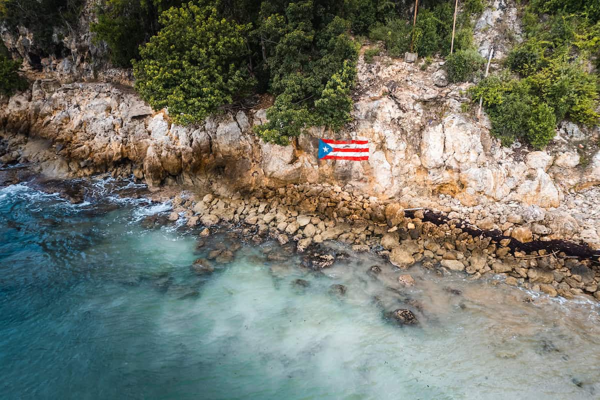 A rock cliff along the ocean with a Puerto Rican flag painted on it.